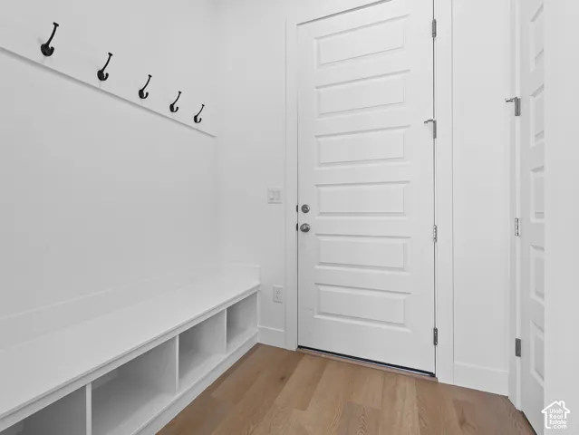 Built-in storage bench with lower cubbies, wall-mounted matte black coat hooks, and wood-finish flooring