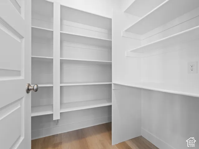 Custom walk-in storage area featuring white built-in shelving, wood-finish flooring, and a dedicated electrical outlet