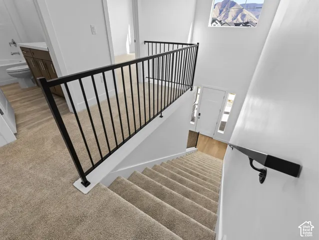 Staircase featuring neutral carpeting, matte black metal railings, and a wall-mounted handrail, complemented by mountain scenery through the transom window