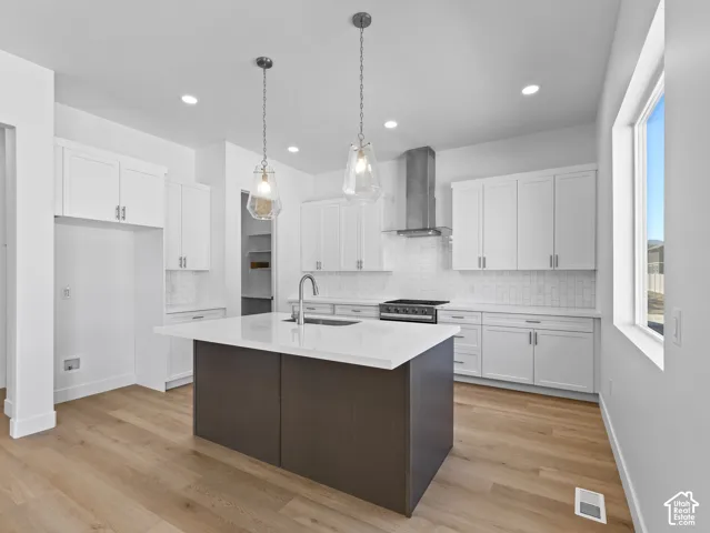 Kitchen featuring white shaker-style cabinetry, quartz countertops, a central island with a contrasting dark wood-finish base, stainless steel range hood, and wood-finish flooring