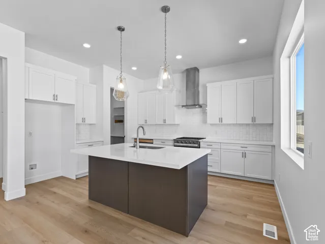 Kitchen featuring white shaker-style cabinetry, quartz countertops, a central island with a deep-toned finish, stainless steel range hood, and wood-finish flooring