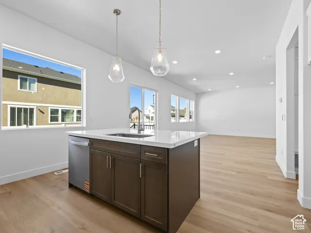 Kitchen island featuring dark wood cabinetry, a light-toned countertop, a stainless steel undermount sink, and dual glass pendant light fixtures, set over light-toned wood-finish flooring
