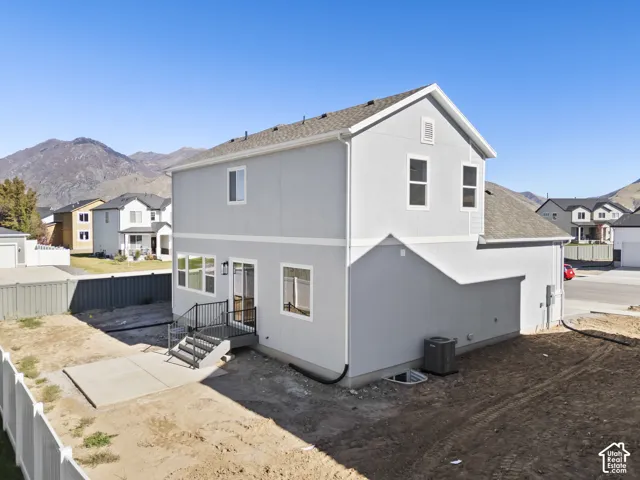Two-story exterior featuring light gray stucco siding, asphalt shingle roofing, concrete patio, metal staircase railing, and mountain backdrop