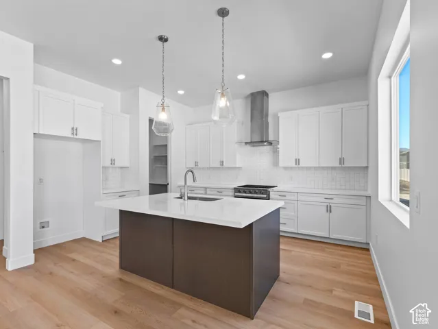 Kitchen featuring an island with a quartz countertop, white shaker-style cabinetry, stainless steel range hood, glass pendant lighting, and wood-finish flooring