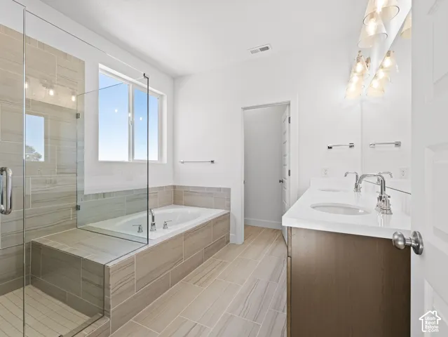 Bathroom featuring a dual-sink vanity with a solid-surface countertop, a glass-enclosed walk-in shower, a soaking tub with tile surround, and horizontal tile flooring
