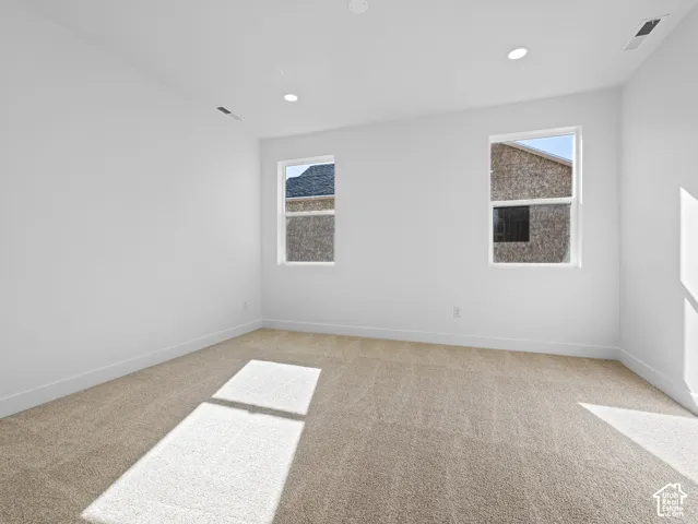 Neutral-toned carpeting, recessed ceiling lighting, and dual windows with white frames
