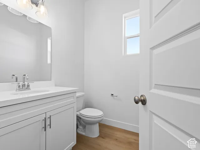White vanity with a solid surface countertop, undermount sink, chrome faucet, wall-to-wall mirror with integrated lighting, and wood-finish flooring