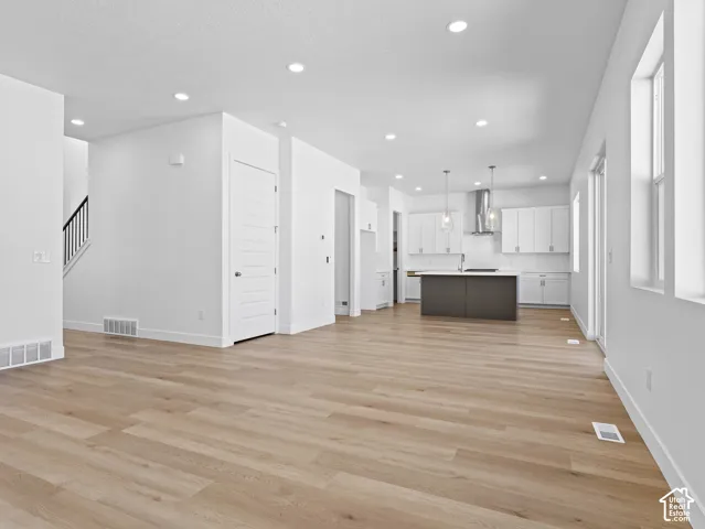 Open-concept interior featuring light wood-finish flooring, recessed lighting, white shaker-style cabinetry, a contrasting kitchen island, and stainless steel chimney-style range hood