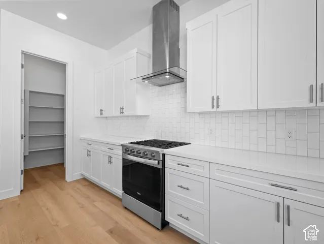 Kitchen featuring white shaker-style cabinetry, quartz countertops, subway tile backsplash, stainless steel chimney-style range hood, and wood-finish flooring