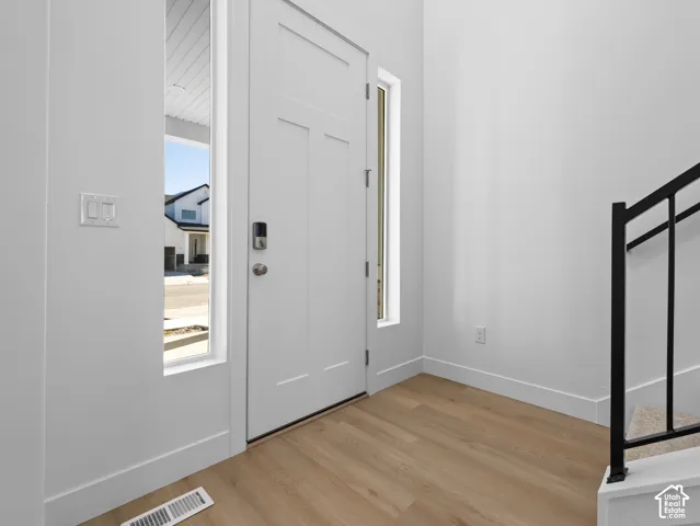 Entryway featuring a solid panel front door, flanking vertical windows, wood-finish flooring, and a metal stair railing