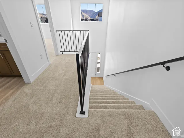 Staircase featuring neutral carpeting, matte black metal balusters, and a matching wall-mounted handrail, complemented by large windows showcasing mountain scenery