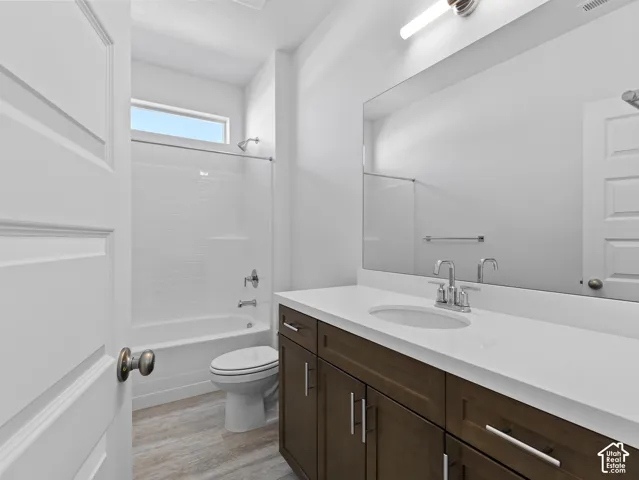 Bathroom featuring a wood-finish vanity with a stone-composite countertop, full-width mirror, inset oval sink, and a combination tub and shower with tile surround