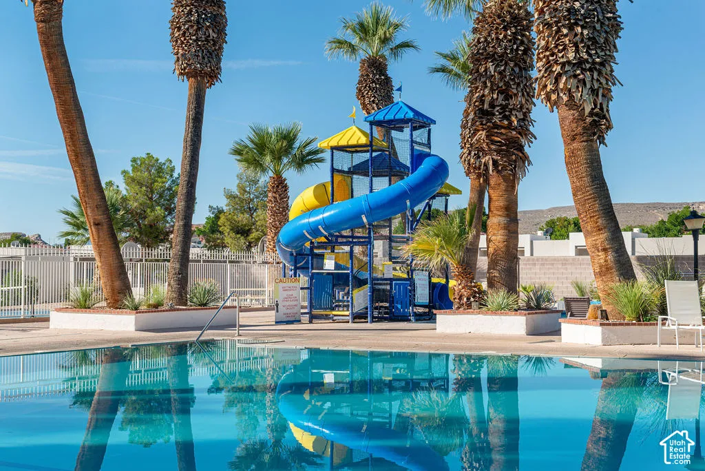 Swimming pool with a water slide structure, surrounded by mature palm trees and desert landscaping