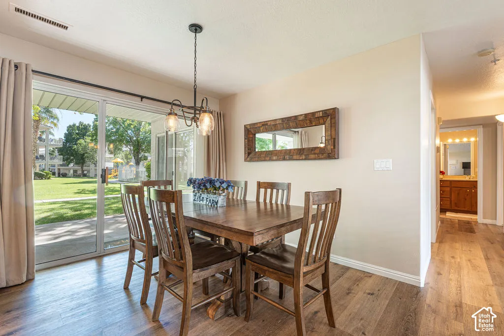 Dining area with wood-finish flooring, a contemporary chandelier, and a sliding glass door opening to a concrete patio and green space