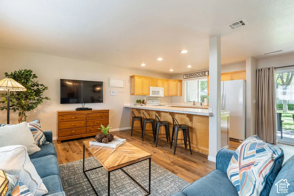 Open-concept living area featuring wood-finish flooring, recessed lighting, a breakfast bar with seating, and light wood cabinetry in the kitchen