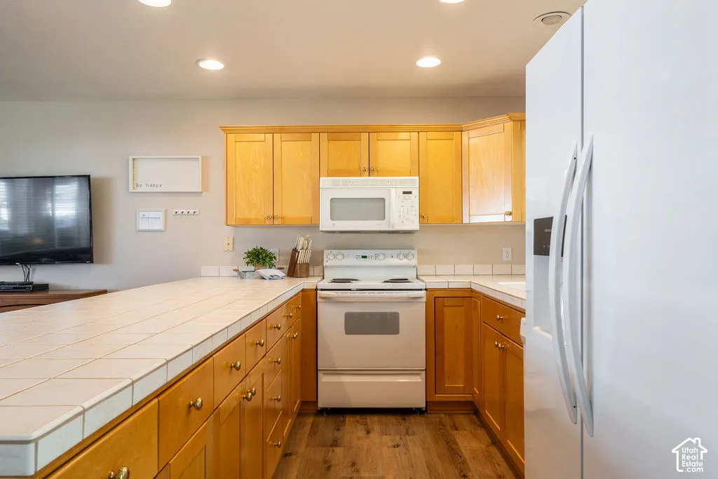 Wood-finish flooring, recessed lighting, and light wood cabinetry with gold-tone hardware
