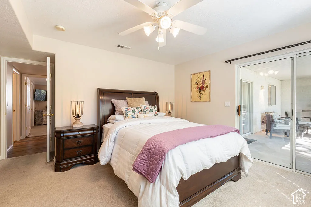 Carpeted room with a ceiling fan, sliding glass door to an outdoor patio, and an interior doorway leading to a hallway with wood-finish flooring