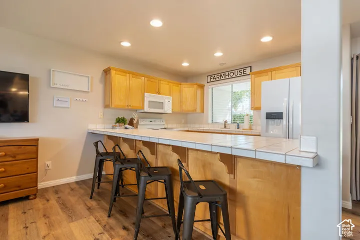 Kitchen with wood-finish flooring, wood cabinetry, built-in microwave, white tile countertops, and recessed lighting