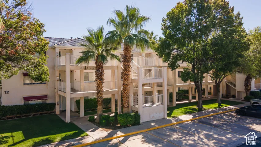 Multi-story building featuring exterior balconies, mature palm trees, and manicured landscaping