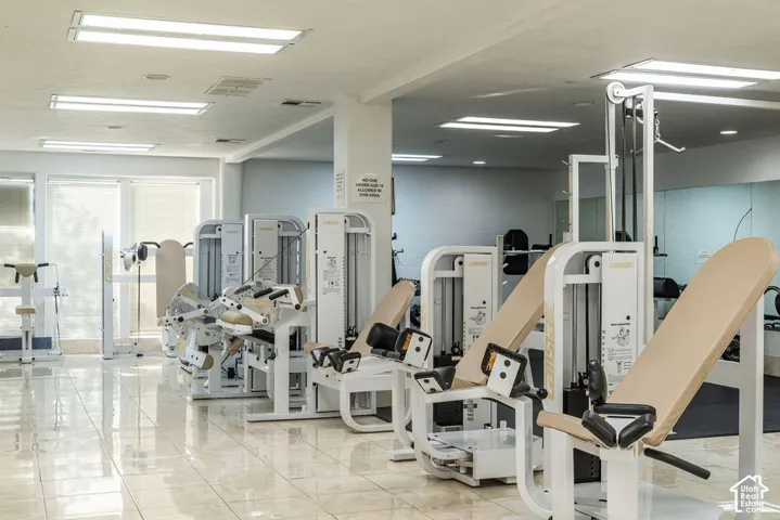 Fitness center featuring multiple weight machines, expansive mirrored wall, large windows with blinds, recessed lighting, and polished tile flooring