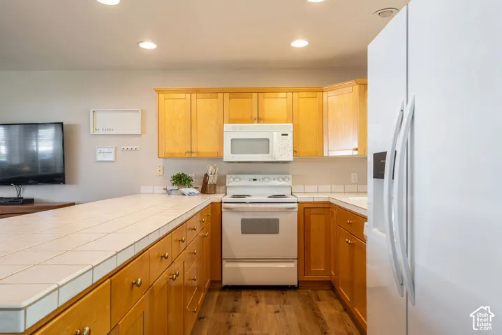 Wood-finish flooring, recessed lighting, and light wood cabinetry with gold-tone hardware