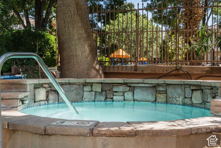 Circular hot tub featuring a stone surround, tiled interior, and a metal handrail