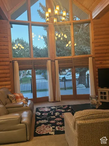 Vaulted log walls, expansive floor-to-ceiling windows, exposed wood ceiling beams, and a tiered wrought-iron chandelier