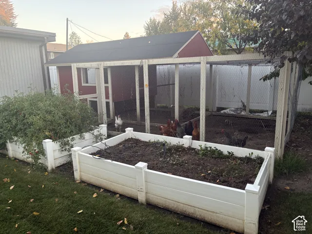 Enclosed coop featuring red siding, a dark roof, and wire mesh fencing, paired with dual elevated white garden beds