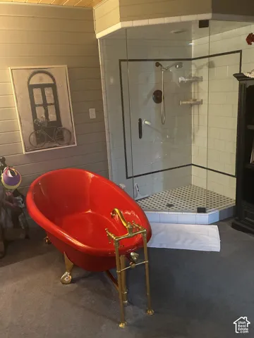 Freestanding soaking tub with a brass finish floor-mount faucet, accompanied by a corner glass-enclosed shower with subway tile surround, mosaic floor tiling, and wood-paneled walls