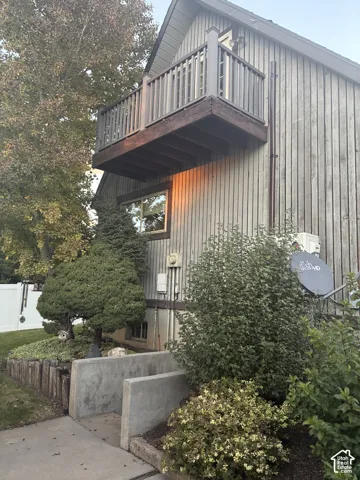 Exterior featuring vertical board-and-batten siding, a second-story cantilevered balcony with wooden railings, and concrete basement stairwell retaining walls