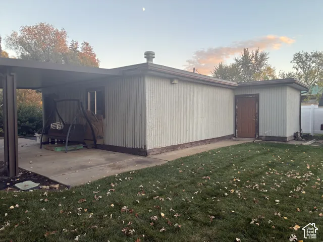 Exterior featuring vertical siding, a covered concrete patio, a detached carport structure, and a lawn