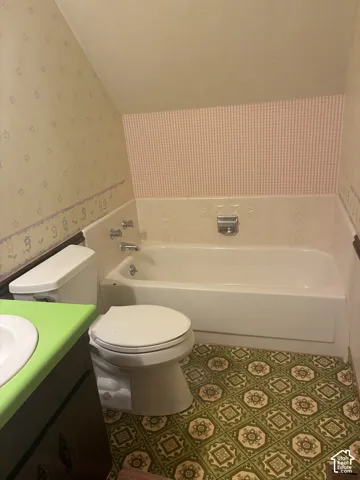 Bathroom featuring a soaking tub with an integrated surround, patterned vinyl flooring, and a vanity cabinet topped with a solid-surface counter and an undermount sink