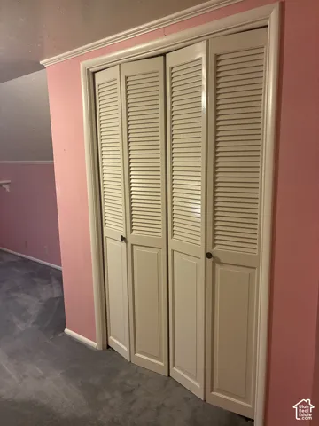 Storage closet featuring four-panel white louvered bifold doors with circular knobs and crown molding