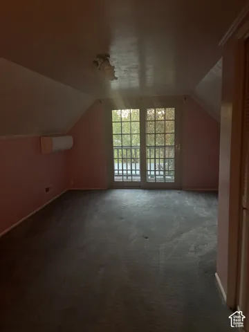 Sloped ceiling room featuring wall-mounted climate control, carpeting, and glass-paneled French doors with exterior railing access