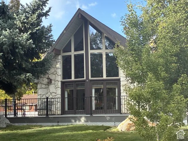 A-frame exterior featuring floor-to-ceiling windows, natural stone masonry, a dark metal railing, and a raised deck