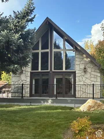 A-frame exterior featuring stone veneer siding, floor-to-ceiling multi-pane windows, and a metal railing