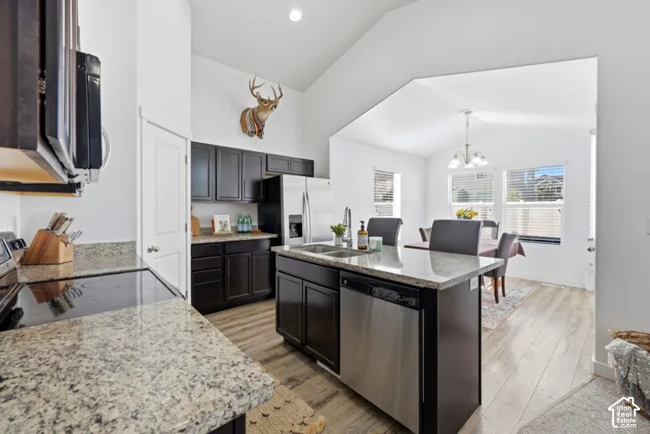 Kitchen featuring dark cabinetry, stone countertops, stainless steel appliances, a central island, and wood-finish flooring under vaulted ceilings