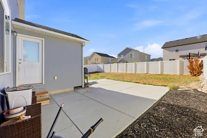 Backyard featuring a concrete patio, white vinyl perimeter fencing, and an exterior door with white trim