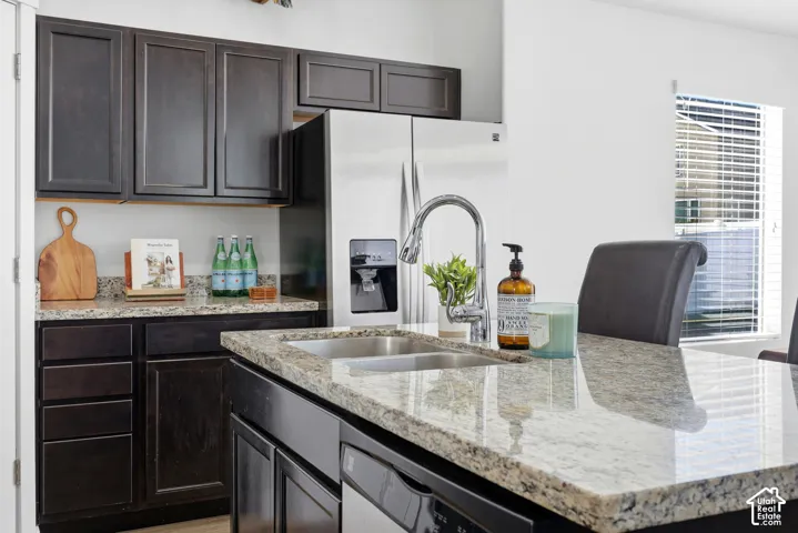 Kitchen featuring dark wood cabinetry, stone countertops, a central island with a double-basin stainless steel sink, a chrome high-arc faucet, and stainless steel appliances