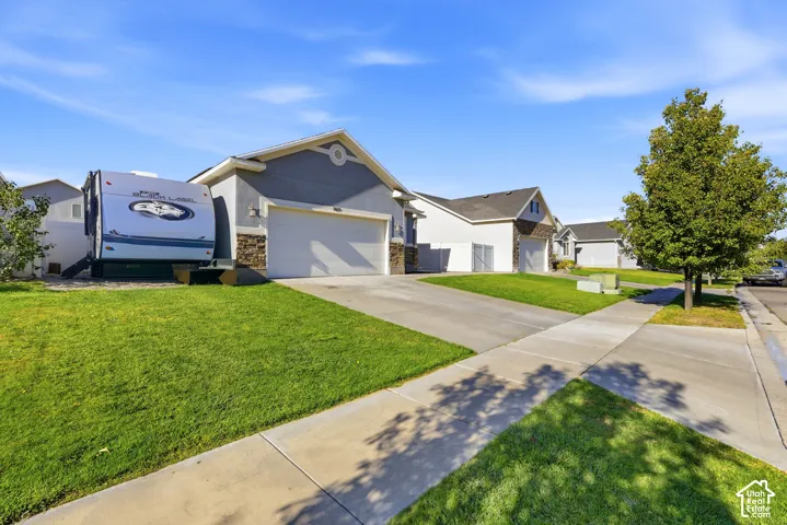 Single-story exterior featuring a stone facade, gabled roofline, concrete driveway, attached multi-car garage, and side yard access