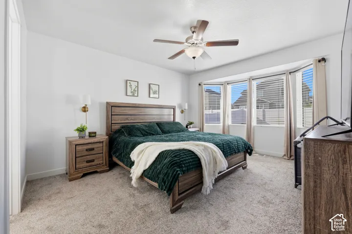 Bedroom featuring wall-to-wall carpeting, a large bay window, a ceiling fan with integrated lighting, and two wall-mounted light fixtures