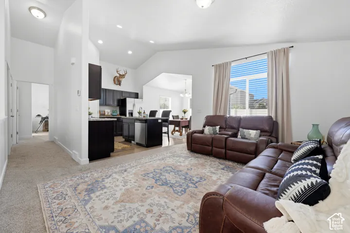 Vaulted ceilings, recessed lighting, and neutral wall color palette, featuring a kitchen island with stone-finish countertops and dark cabinetry