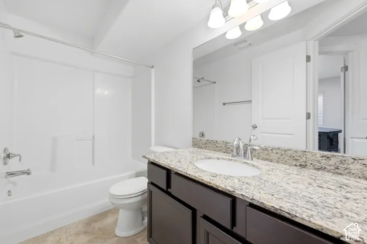 Bathroom featuring a vanity with dark cabinetry, stone-finish countertop, undermount sink, full-width wall mirror, and a shower-tub combination with a white surround