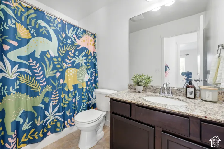 Bathroom featuring a stone-look countertop, undermount oval sink, dark wood-finish cabinetry, wall-to-wall vanity mirror, and three-bulb vanity lighting