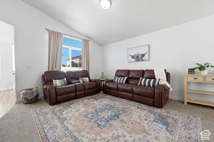 Vaulted ceilings, neutral wall palette, wall-to-wall carpeting, and a large window featuring horizontal blinds