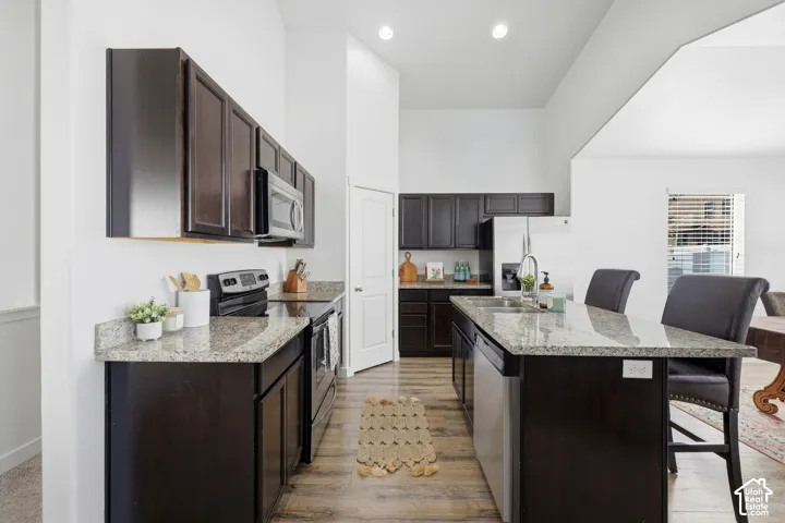 Kitchen featuring dark cabinetry, stone countertops, stainless steel appliances, a center island with a breakfast bar, and wood-finish flooring