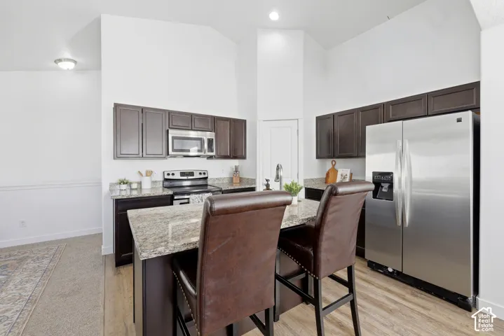 Kitchen featuring dark wood cabinetry, stone countertops, stainless steel appliances, a center island with bar seating, and vaulted ceilings
