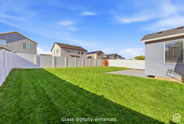 Private backyard featuring a manicured lawn, concrete patio, and white vinyl perimeter fencing