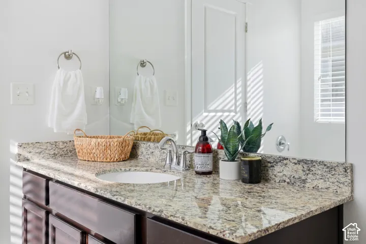 Dark-toned cabinetry featuring an integrated stone countertop, undermount sink, dual-handle polished chrome faucet, and large-scale wall mirror
