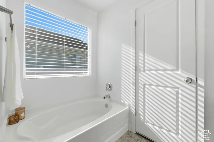 Deep soaking tub with a chrome single-handle faucet and integrated overflow drain, featuring a rectangular window with horizontal blinds and a two-panel interior door with a circular knob